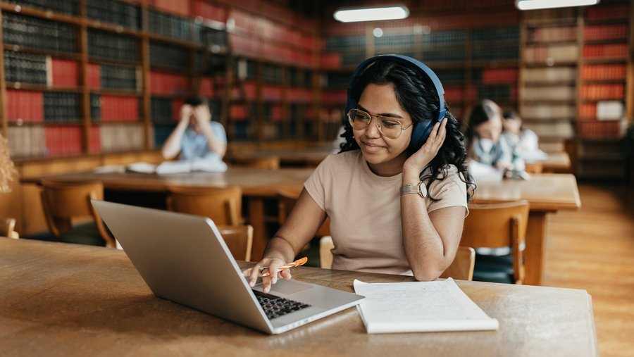 Girl with headphones studying on laptop in library
